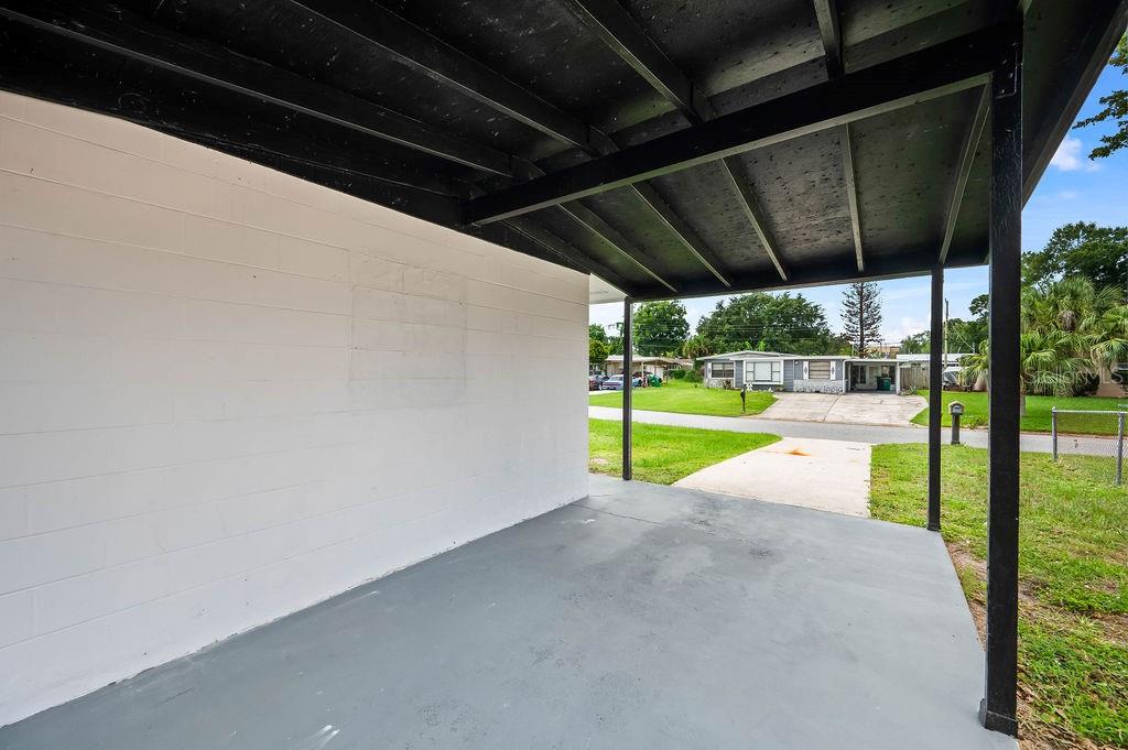 A covered concrete carport features a white block wall and a black wooden ceiling — 2204 SHELBY DRIVE, MELBOURNE, FL