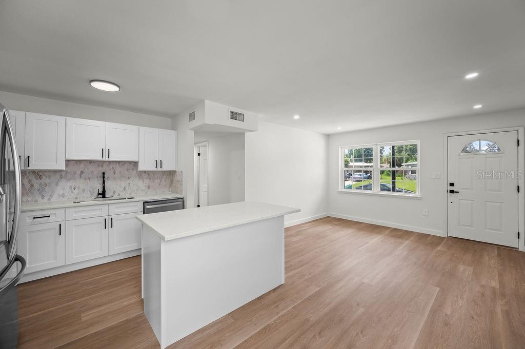 A kitchen and living area with white cabinets, a central island, and light wood flooring — 2204 SHELBY DRIVE, MELBOURNE, FL
