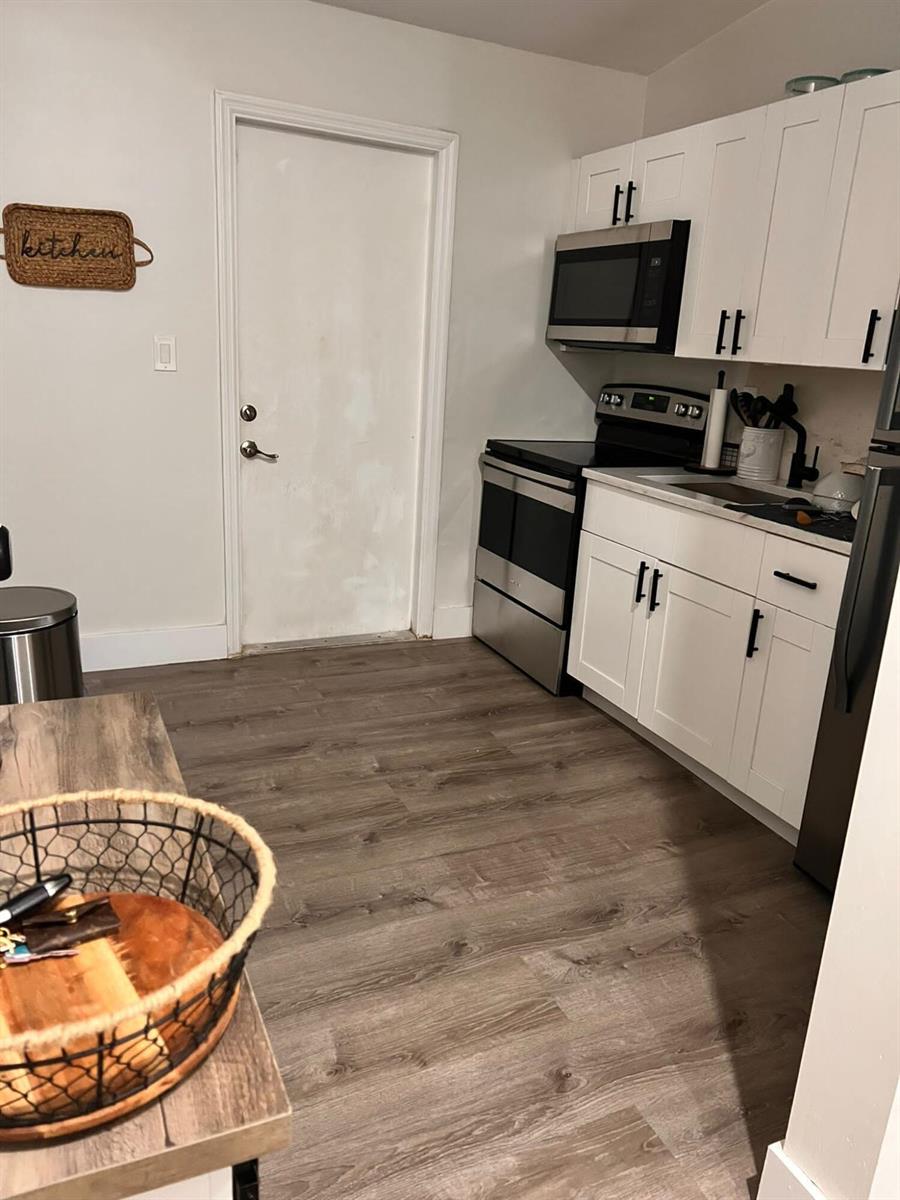 A kitchen features white cabinets, stainless steel appliances, and wood-look flooring — 555 NW 15th Court, Pompano Beach FL 33060, POMPANO BEACH, FL