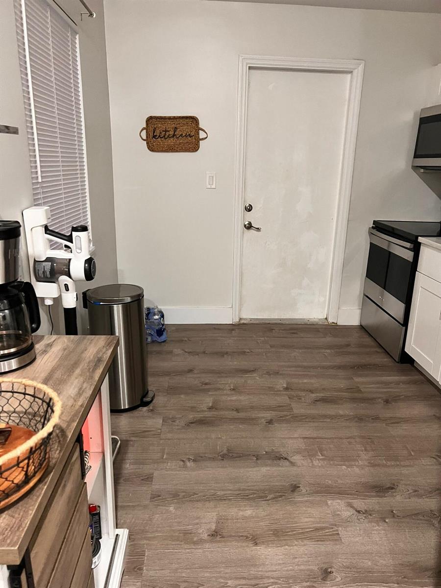 A kitchen features wood-look flooring, stainless steel appliances, a white door, and a wall sign — 555 NW 15th Court, Pompano Beach FL 33060, POMPANO BEACH, FL