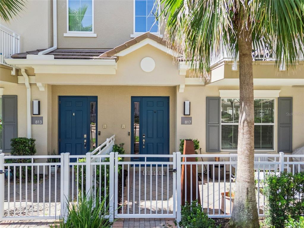 A white fence encloses the front patio and blue entry doors of a two-story townhouse — 817 GREYBULL RUN, LAKE MARY, FL