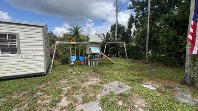 A backyard features a small shed, a wooden playset with swings, and a grassy lawn — 3000 N 72nd Way, Hollywood FL 33024, HOLLYWOOD, FL