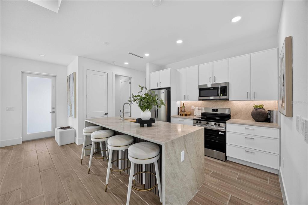 A modern kitchen features a stone-topped island with bar seating, white cabinetry, and wood-look flooring — 16213 CASHMERE AVENUE, PORT CHARLOTTE, FL