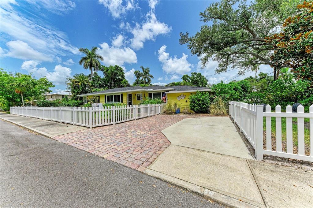 A yellow single-story house features a brick driveway and a white picket fence — 405 20TH STREET W, BRADENTON, FL