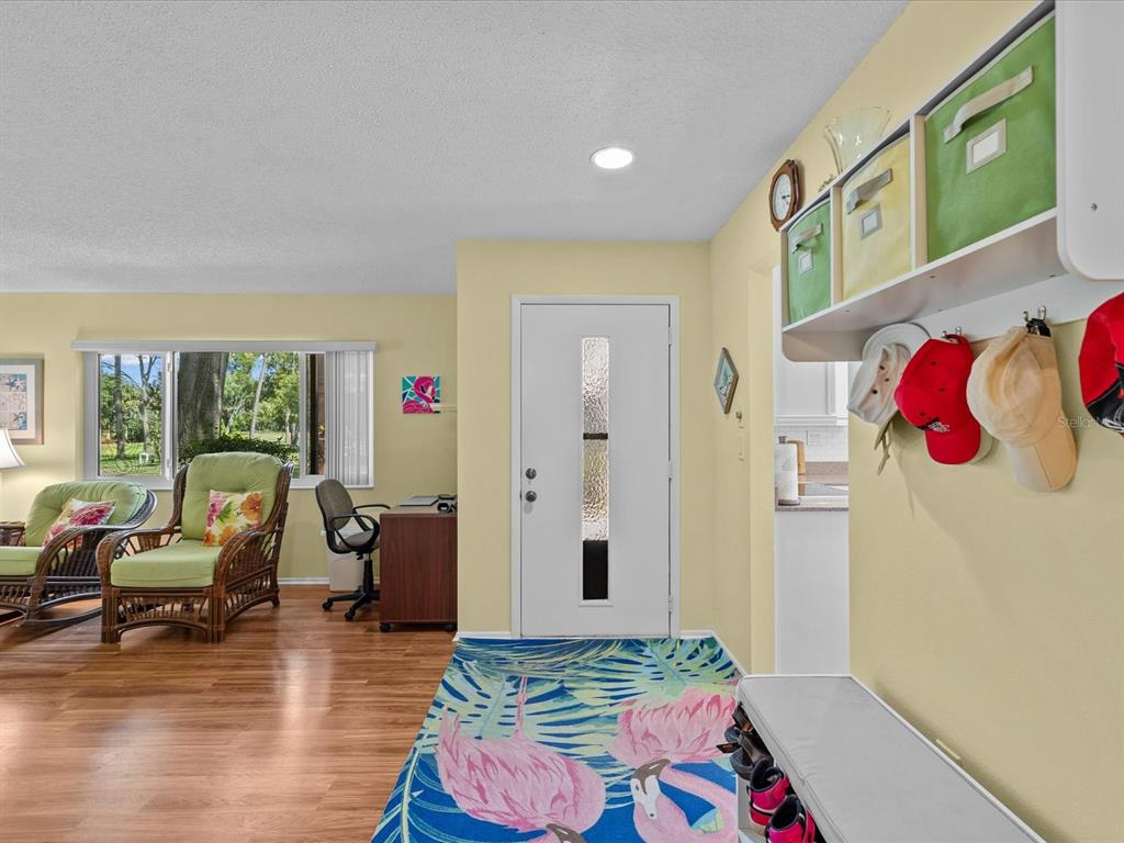 An entryway features a flamingo-patterned rug, a white front door, and wall-mounted storage bins — 13002 WEDGEWOOD WAY UNIT B, HUDSON, FL