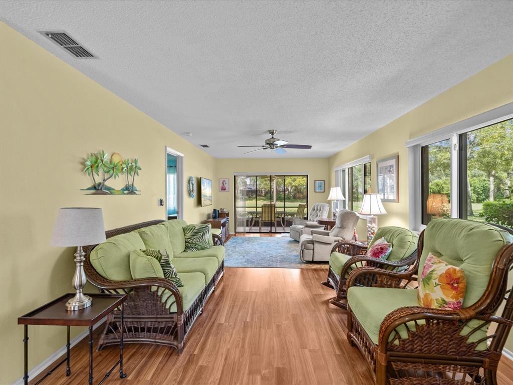 A living room features light yellow walls, wicker furniture, wood-look flooring, and a sliding glass door — 13002 WEDGEWOOD WAY UNIT B, HUDSON, FL