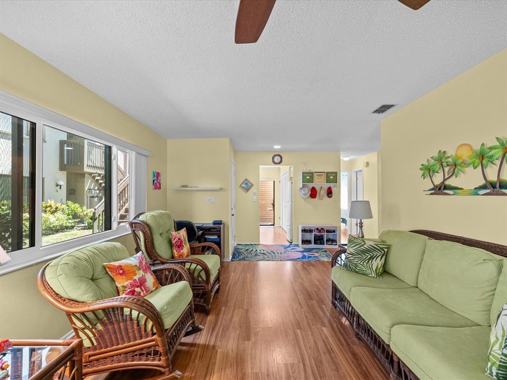 A living room features light yellow walls, wood-look flooring, wicker furniture, and a large window — 13002 WEDGEWOOD WAY UNIT B, HUDSON, FL