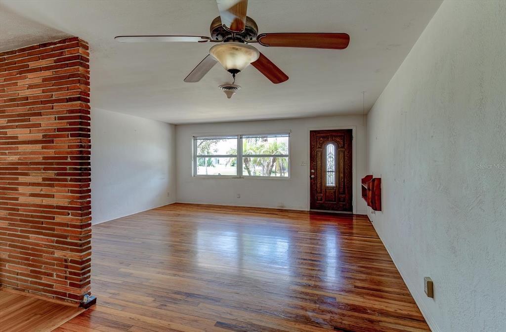 A living room features hardwood floors, a brick accent wall, a ceiling fan, and a door — 3841 CARDINAL BOULEVARD, PORT ORANGE, FL
