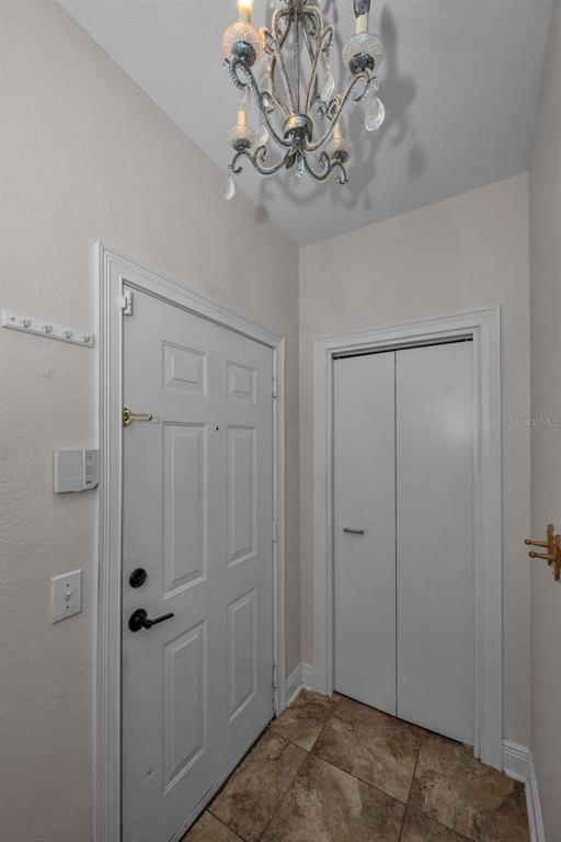 An entryway features a white front door, a bifold closet door, and a decorative chandelier — 2199 CHIANTI PLACE UNIT 9-0925, PALM HARBOR, FL