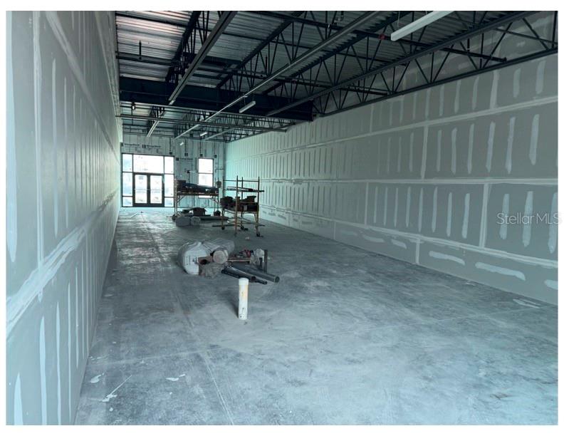 An unfinished commercial interior space features exposed ceiling trusses, drywall-covered walls, and concrete flooring — 6355 INITIATIVE BOULEVARD UNIT 110, SARASOTA, FL
