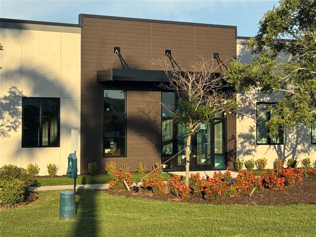 A modern commercial building exterior features dark wood-look siding, a black awning, and landscaped gardens — 6355 INITIATIVE BOULEVARD UNIT 110, SARASOTA, FL