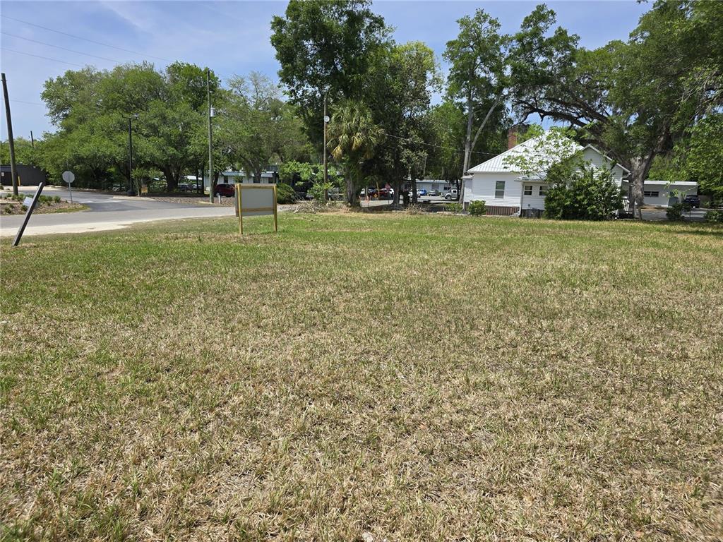 A vacant, grassy lot with a wooden sign stands near a road and mature trees — 33 NW 3RD STREET, WILLISTON, FL