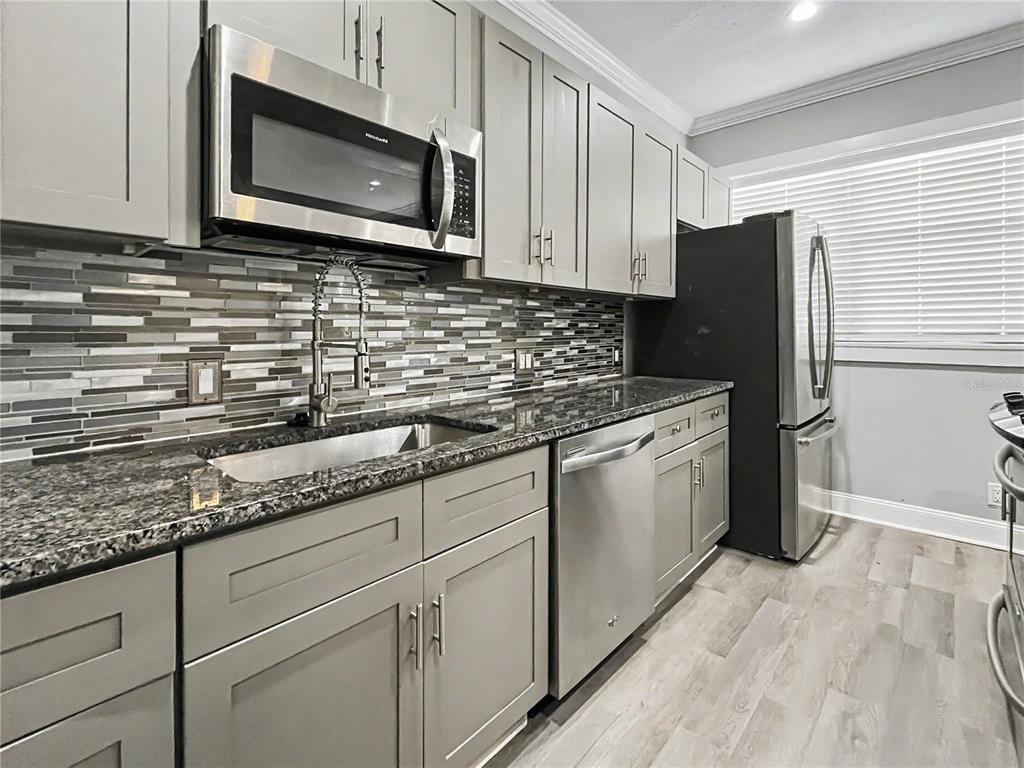 A kitchen features gray shaker cabinets, stainless steel appliances, granite countertops, and a mosaic tile backsplash — 408 ARMADA ROAD S UNIT 2, VENICE, FL
