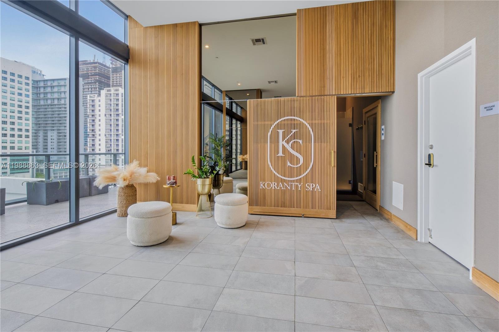 A spa reception area features slatted wood walls, two white ottomans, and floor-to-ceiling windows — 239 SW 9th St # 802, Miami FL 33130, MIAMI, FL