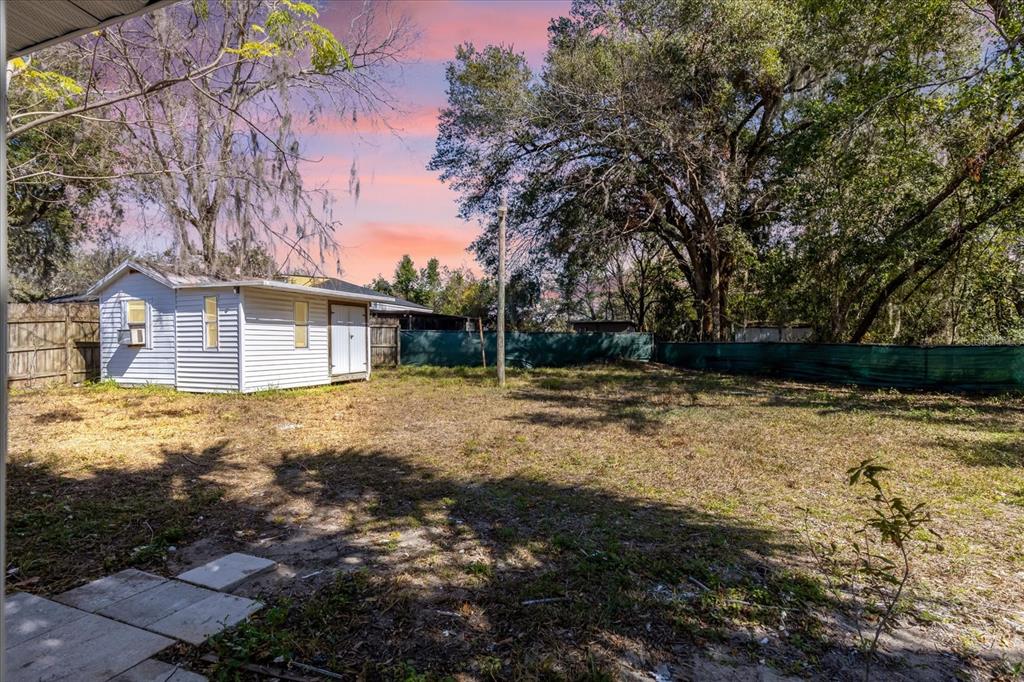 A white shed sits in a grassy backyard enclosed by a wooden and green fence — 204 LOUIS STREET, LEESBURG, FL