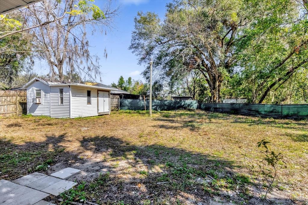 A white shed sits in a grassy backyard enclosed by a wooden and green fence — 204 LOUIS STREET, LEESBURG, FL