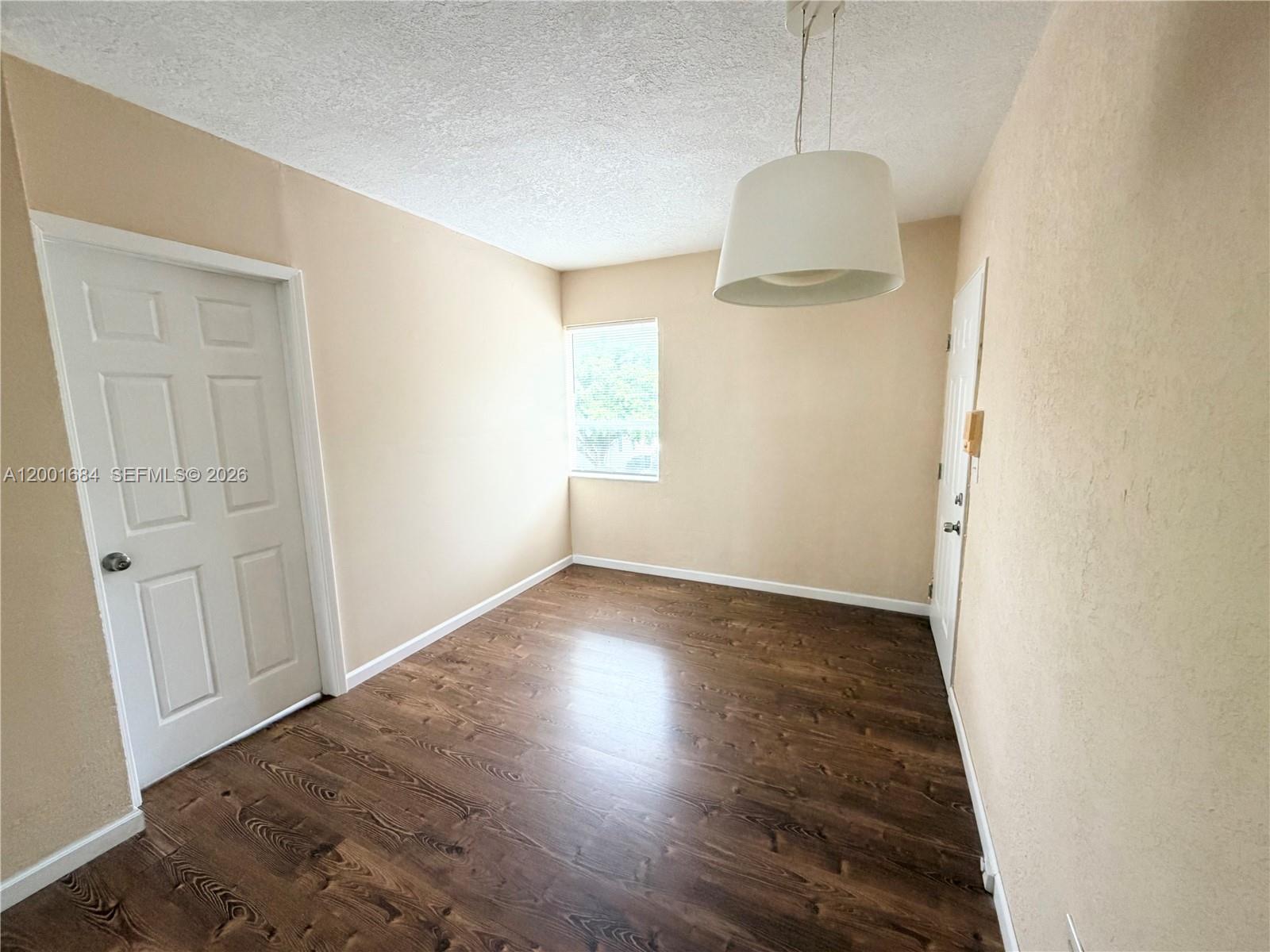 An empty room features beige walls, dark wood-look flooring, a white door, and a pendant light — 620 84th St # 25, Miami Beach FL 33141, MIAMI BEACH, FL