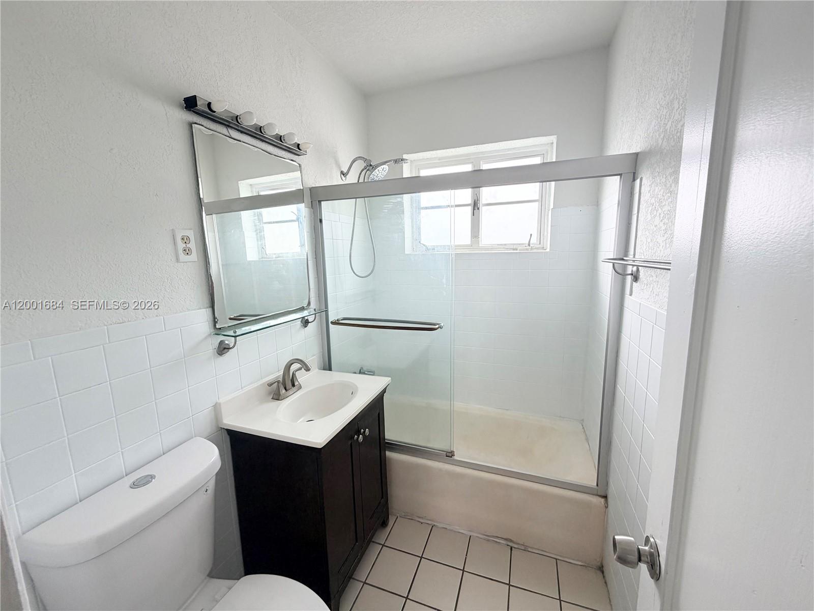 A bathroom features a white toilet, a dark vanity, and a glass-enclosed shower-tub combination — 620 84th St # 25, Miami Beach FL 33141, MIAMI BEACH, FL