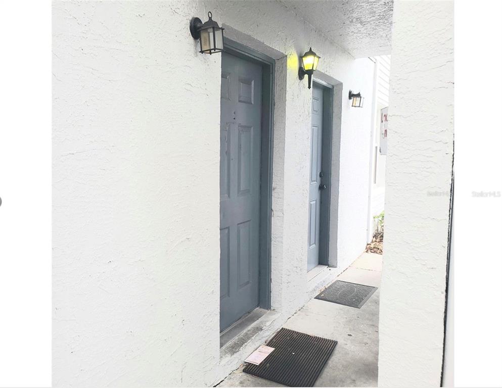 Two gray doors with exterior wall lamps are set along a white stucco walkway — 7100 WATERSIDE DRIVE, TAMPA, FL