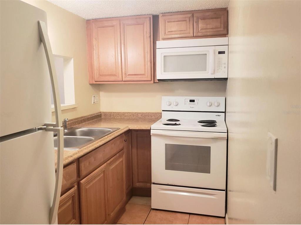 A small kitchen features light wood cabinets, white appliances, and tan laminate countertops — 7100 WATERSIDE DRIVE, TAMPA, FL
