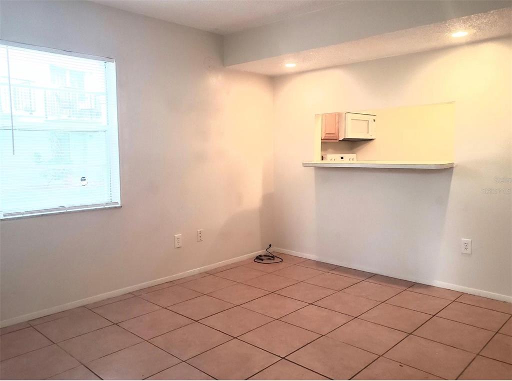 An empty room with tiled floors, a window, and a pass-through opening to a kitchen — 7100 WATERSIDE DRIVE, TAMPA, FL