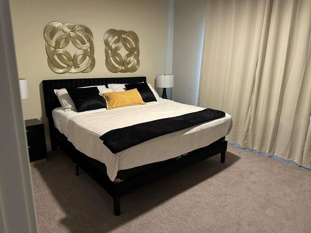 A bedroom features a black bed frame, white bedding, gold wall art, and beige curtains — 7760 SANDY RIDGE DRIVE UNIT 115, REUNION, FL