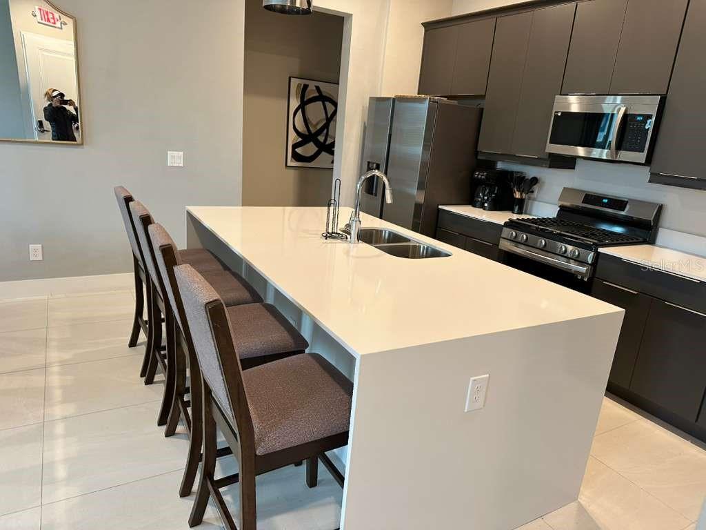 A modern kitchen features a large white quartz island with bar seating and dark cabinetry — 7760 SANDY RIDGE DRIVE UNIT 115, REUNION, FL