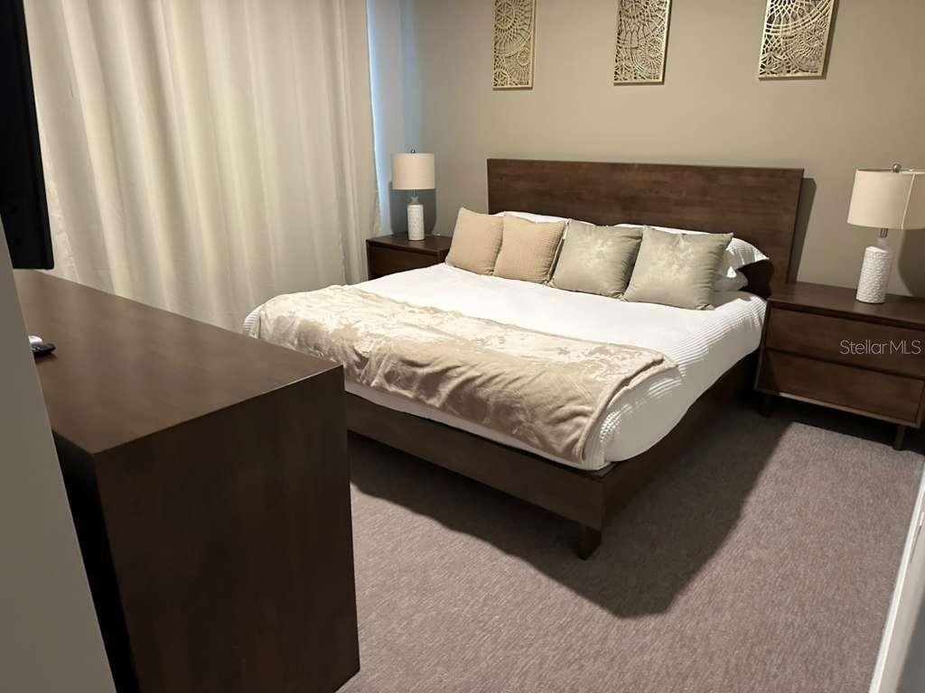 A bedroom features a wooden bed frame, two nightstands with lamps, and wall-mounted art — 7760 SANDY RIDGE DRIVE UNIT 115, REUNION, FL
