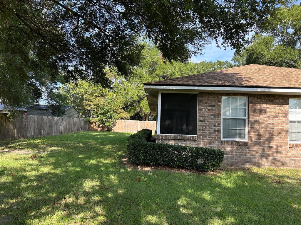 A brick house exterior features a screened-in porch and a large, grassy backyard — 25459 SW 20TH PLACE, NEWBERRY, FL