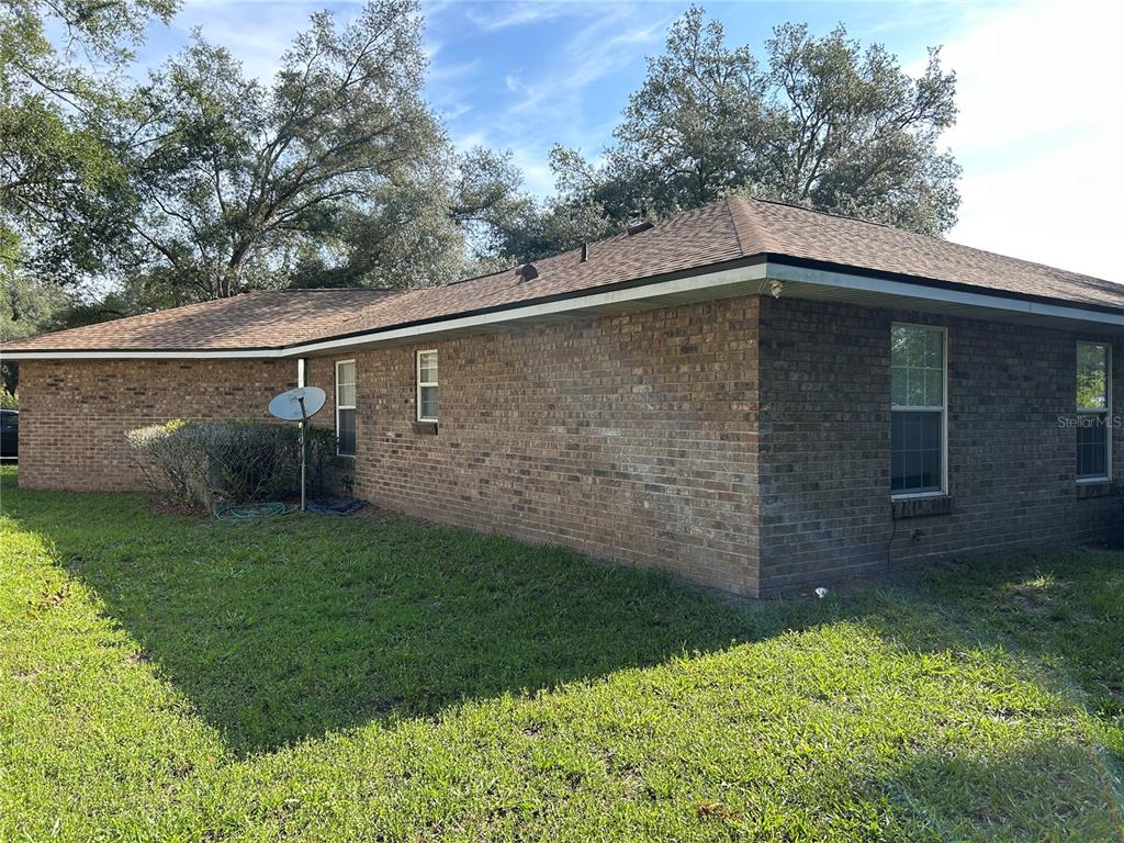 A side view of a single-story brick house with a hip roof and lawn — 25459 SW 20TH PLACE, NEWBERRY, FL
