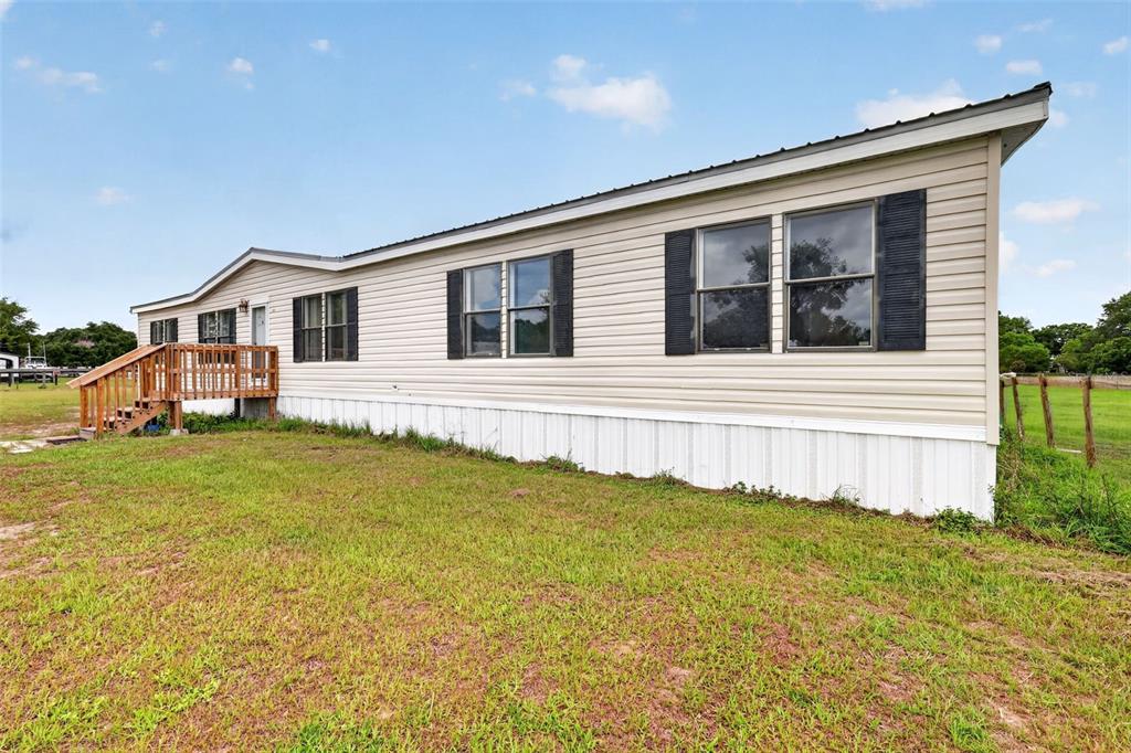 A beige single-wide manufactured home with a wooden deck sits on a grassy lot — 311 SE HIGHWAY 42, SUMMERFIELD, FL