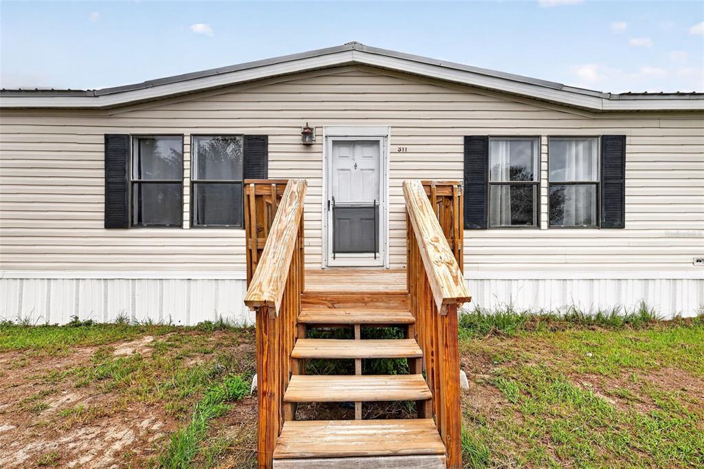 A single-story manufactured home with beige siding and a wooden staircase leading to the entrance — 311 SE HIGHWAY 42, SUMMERFIELD, FL