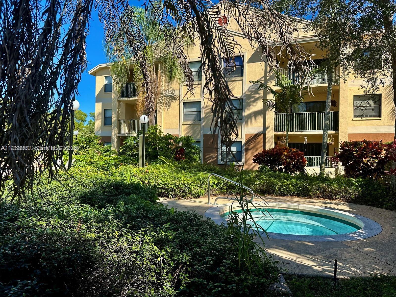 A small circular hot tub sits in a landscaped courtyard outside a multi-story apartment building — 9999 Summwebreeze  Dr # 101, Sunrise FL 33322, SUNRISE, FL
