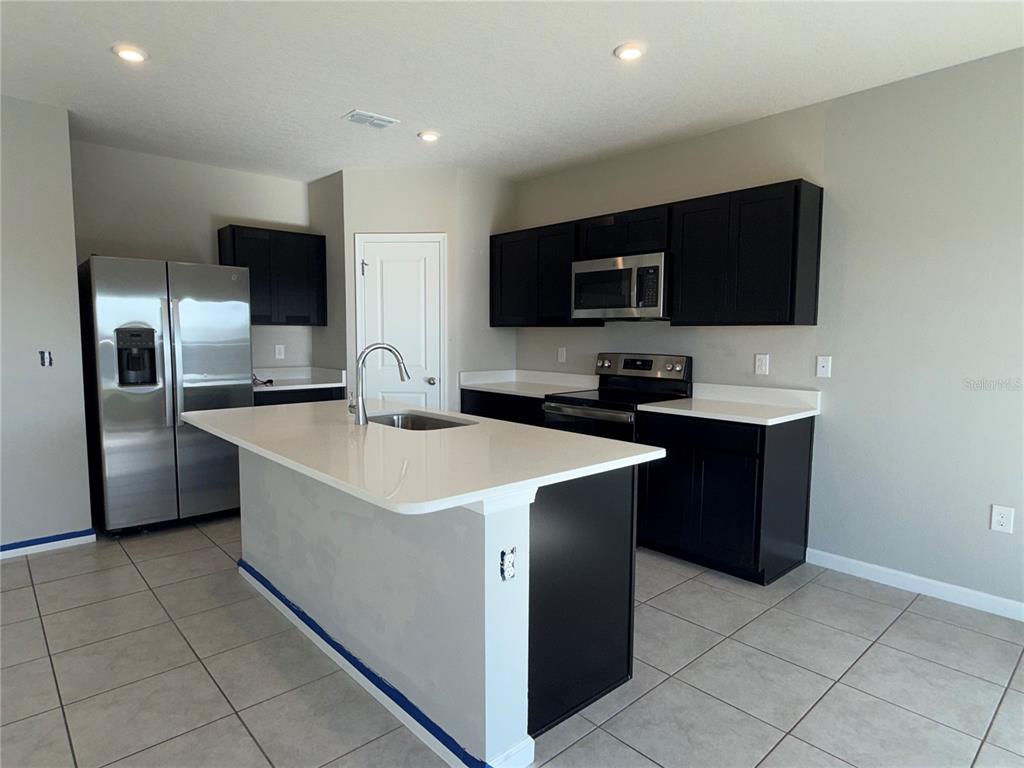 A kitchen features dark cabinets, white countertops, stainless steel appliances, and a central island — 1109 LEXINGTON LANE, HAINES CITY, FL