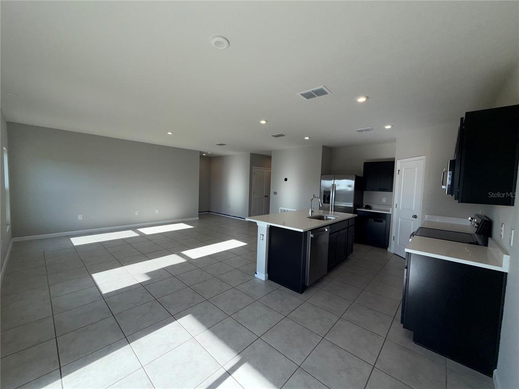An open-concept kitchen with dark cabinets and a central island overlooks a tiled living area — 1109 LEXINGTON LANE, HAINES CITY, FL