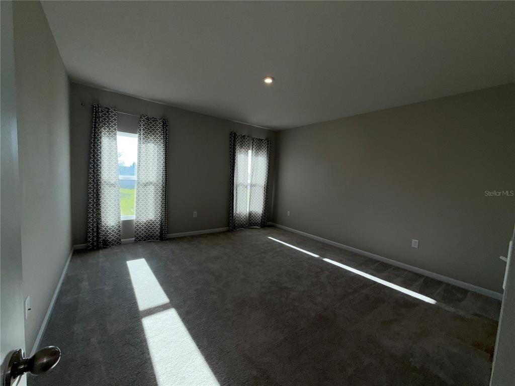 An empty bedroom features gray carpet, neutral walls, and two windows with patterned curtains — 1109 LEXINGTON LANE, HAINES CITY, FL