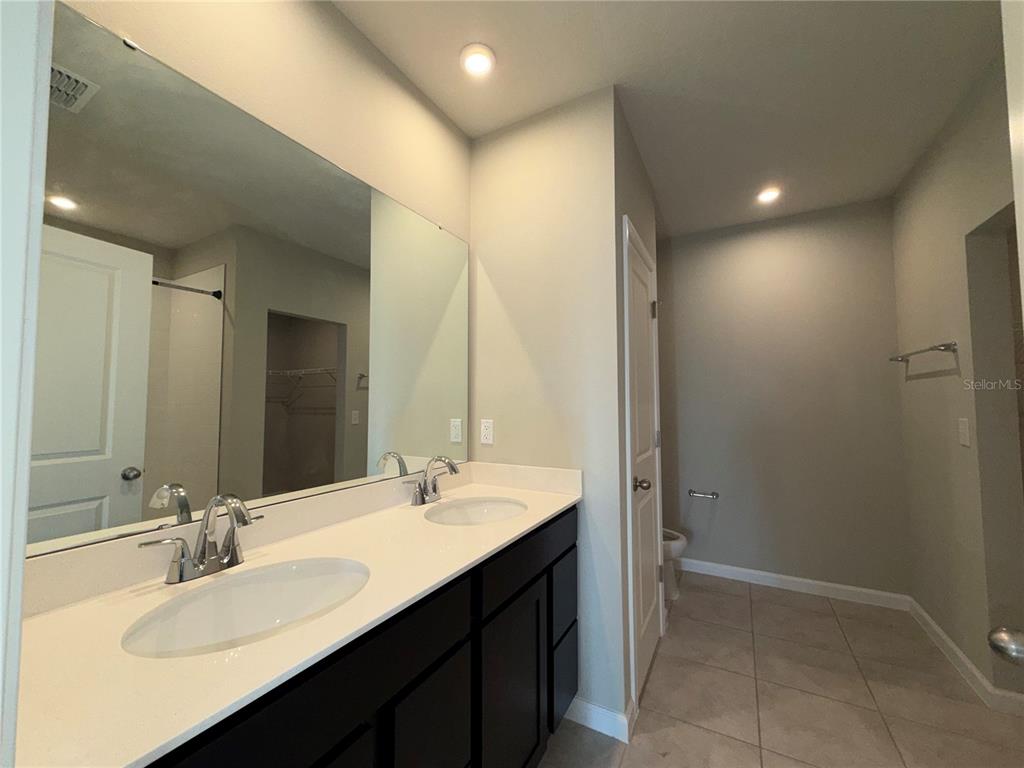A bathroom features a double-sink vanity with dark cabinets, a large mirror, and tile flooring — 1109 LEXINGTON LANE, HAINES CITY, FL