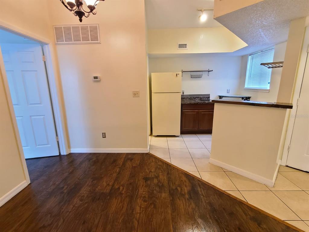 A dining area with wood-look flooring transitions into a tiled kitchen with white appliances — 1948 LAKE ATRIUMS CIRCLE UNIT 121, ORLANDO, FL