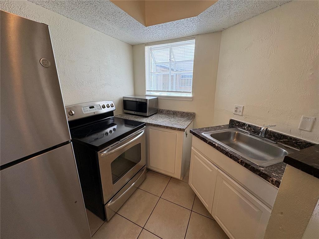 A small kitchen features stainless steel appliances, white cabinets, and dark granite countertops — 1948 LAKE ATRIUMS CIRCLE UNIT 121, ORLANDO, FL