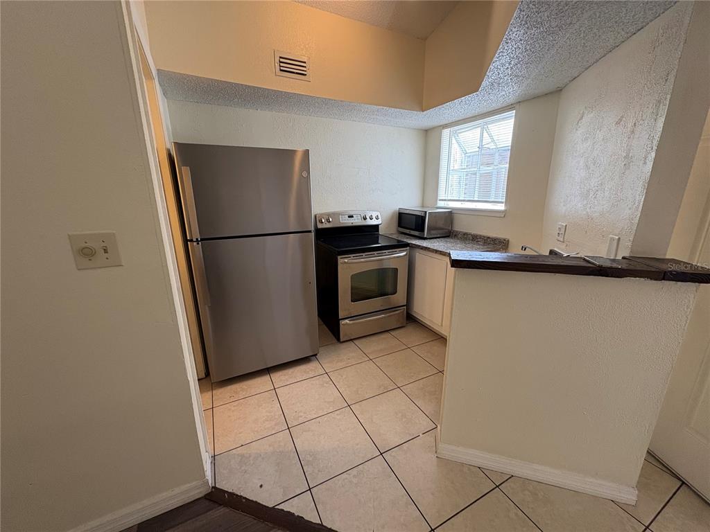 A kitchen features a stainless steel refrigerator, a stove, tiled flooring, and a window — 1948 LAKE ATRIUMS CIRCLE UNIT 121, ORLANDO, FL