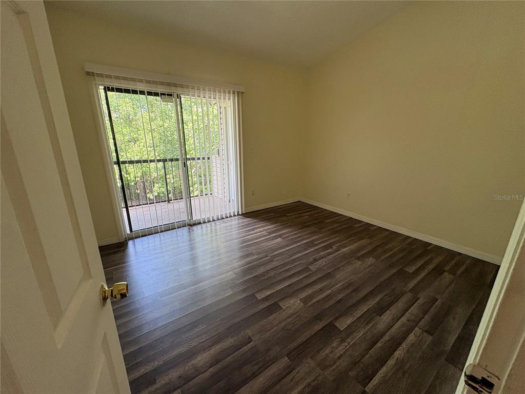 An empty bedroom features wood-look flooring, light-colored walls, and a sliding glass door to a balcony — 1948 LAKE ATRIUMS CIRCLE UNIT 121, ORLANDO, FL