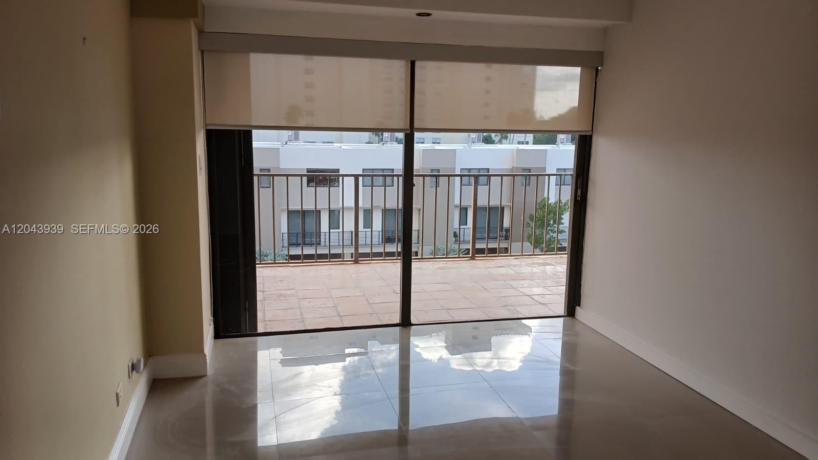 An empty room with glossy tile floors leads to a balcony through sliding glass doors — 1800 NE 114th St # 508, Miami FL 33181, MIAMI, FL