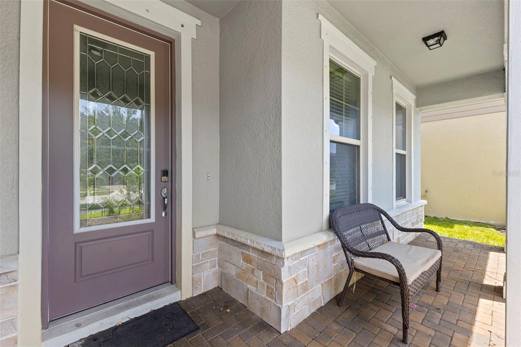 A covered front porch features a brown door, stone accents, and a wicker bench — 18935 BIRCHWOOD GROVES DRIVE, LUTZ, FL