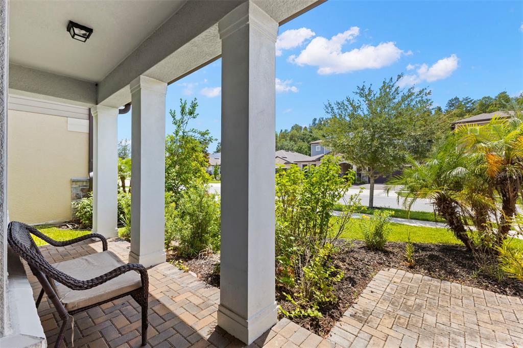 A covered brick patio features white columns, a wicker chair, and a view of landscaping — 18935 BIRCHWOOD GROVES DRIVE, LUTZ, FL