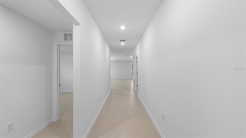 A long, narrow hallway with light-colored tile flooring and white walls leads to an open area — 21237 MULBERRY AVENUE, PORT CHARLOTTE, FL