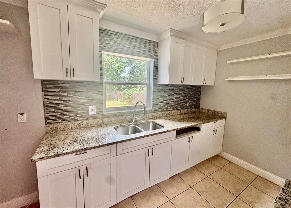 A kitchen features white cabinets, granite countertops, a tiled backsplash, and a double-basin sink — 2006 SARAZEN DRIVE, ORLANDO, FL