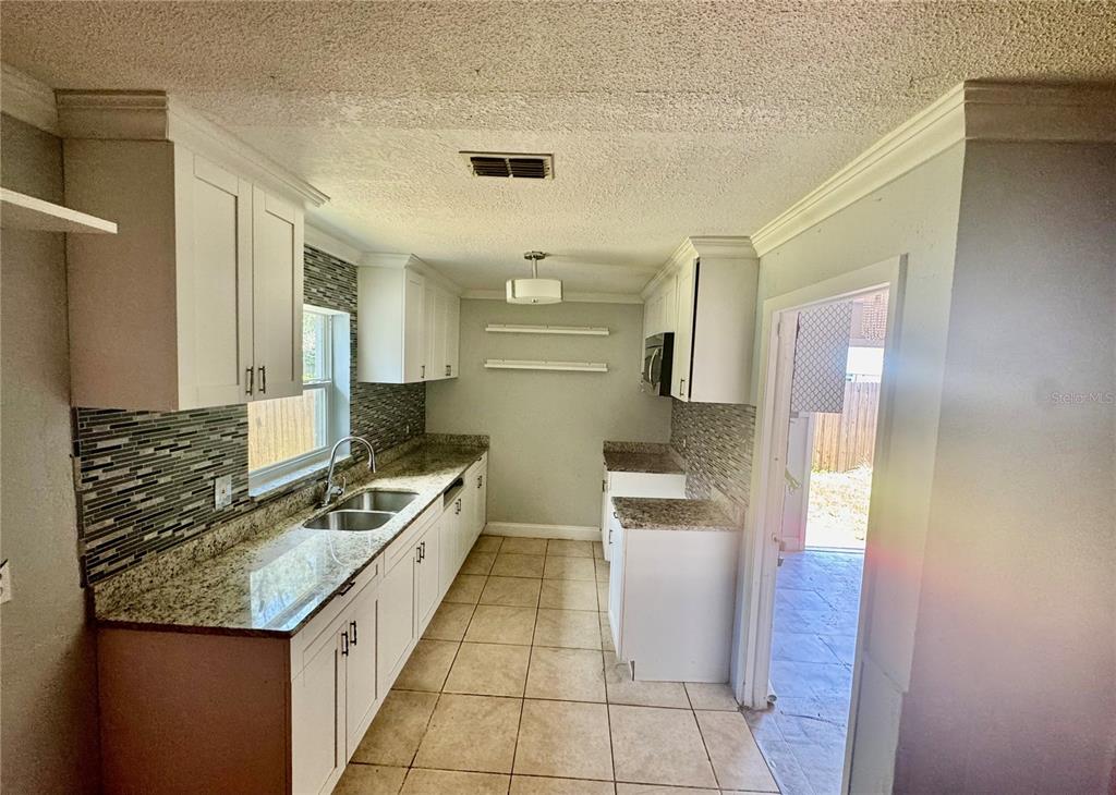A galley kitchen features white cabinets, granite countertops, a tiled backsplash, and light floor tiles — 2006 SARAZEN DRIVE, ORLANDO, FL