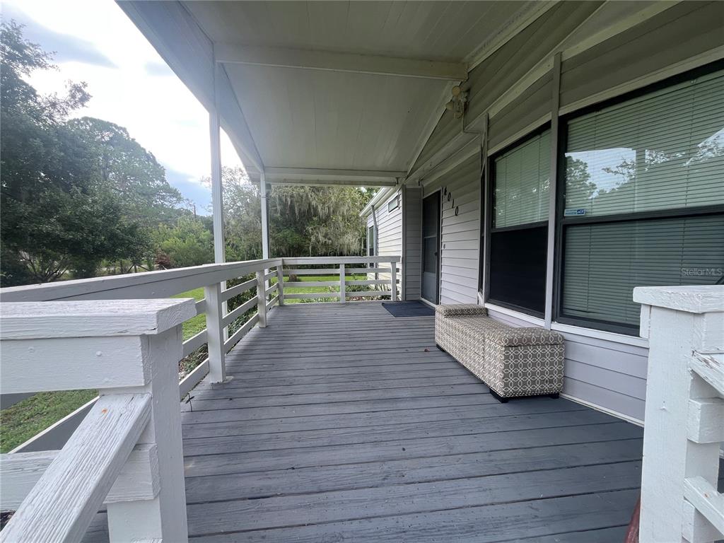 A covered wooden porch features a railing, a patterned bench, and light-colored siding — 4010 GLEN ROAD, LAKELAND, FL
