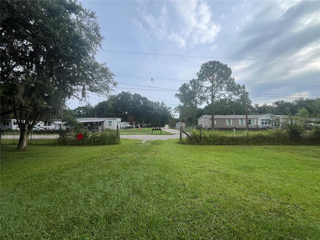 A grassy yard leads to a gated entrance with mobile homes visible in the background — 4010 GLEN ROAD, LAKELAND, FL