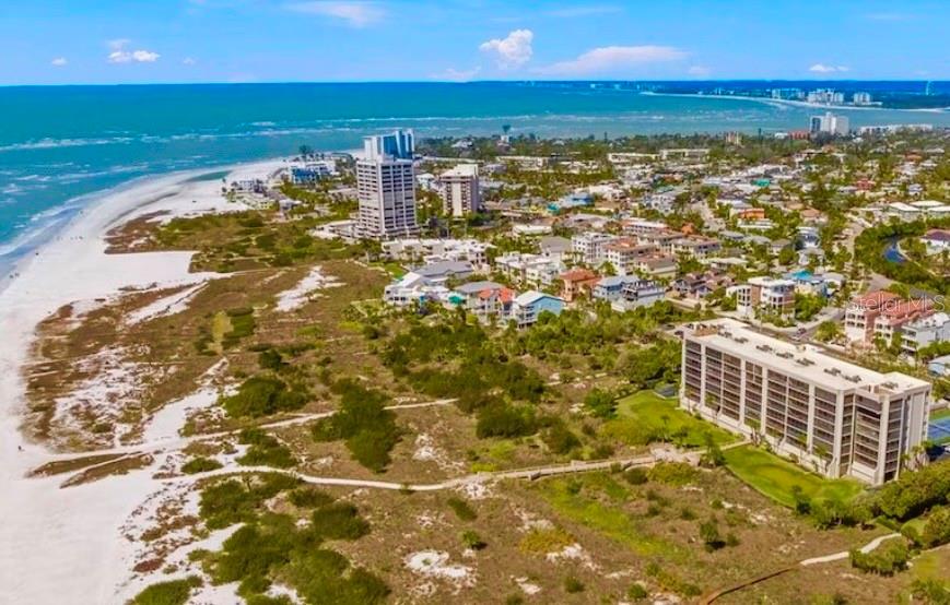 An aerial view shows a sandy beach, coastal vegetation, and several multi-story residential buildings — 420 BEACH ROAD UNIT 606, SARASOTA, FL